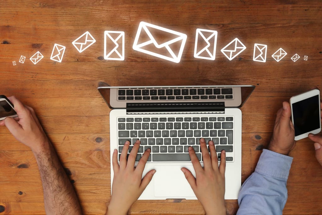 Marketing Strategies for Therapists. Two individuals working at a wooden desk with a laptop and smartphone, surrounded by floating email icons, symbolizing digital communication.